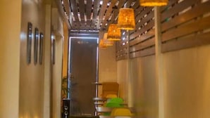 Un couloir recouvert d’une moquette verte mène à un espace détente avec des tables et des chaises.