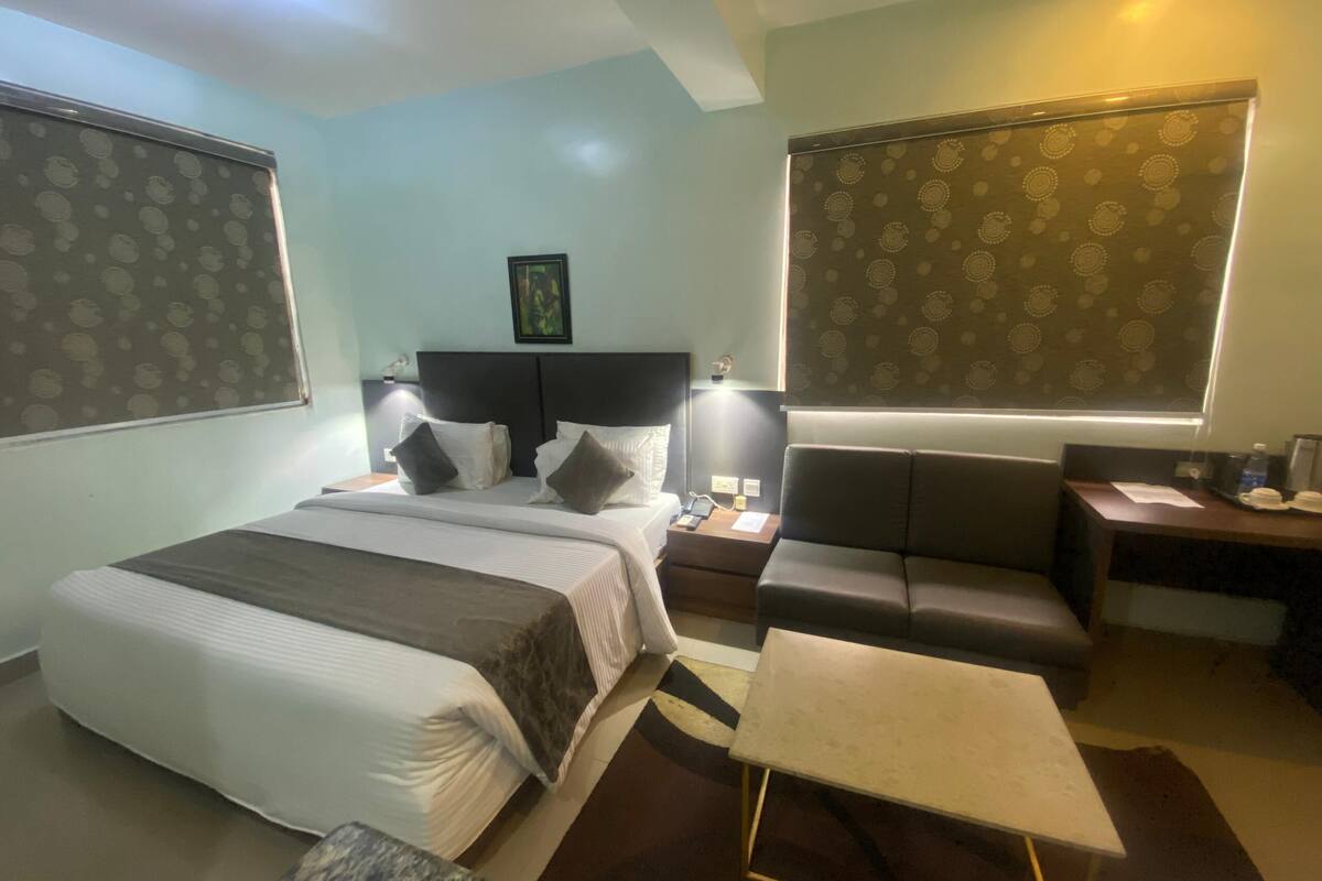 A hotel room with a bed, bedside table, lamp, seating area, and a desk.