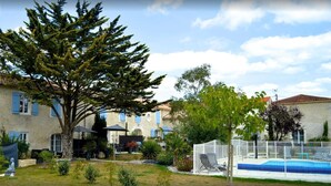 A courtyard with a swimming pool, a large tree, and a building with blue shutters. - Plume 4* charming gites with swimming pool, golf practice and children's playground (Chambon)