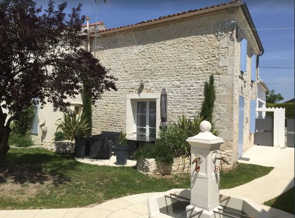 A stone building with a rustic exterior, a small garden with potted plants, and a fountain in the foreground.