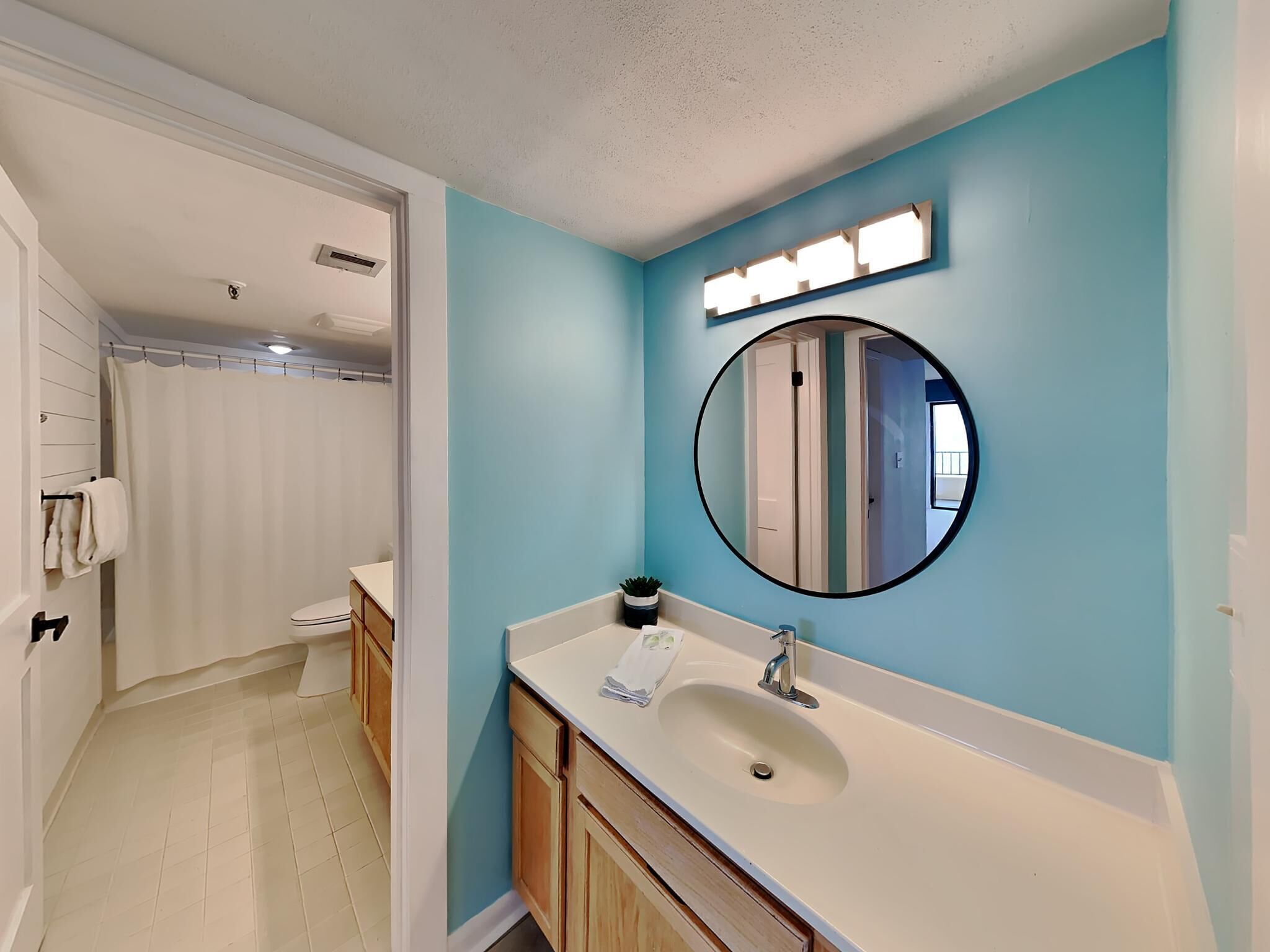 A bathroom with a white sink, a round mirror, and a blue accent wall.