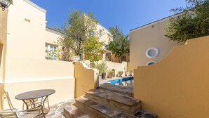 A courtyard with stone steps leading to a pool, surrounded by beige walls and trees. - Vintage Nook 1 Bedroom Apartment in Green Point (Cape Town)