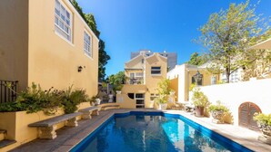 A swimming pool surrounded by yellow buildings with a clear blue sky. - Vintage Nook 1 Bedroom Apartment in Green Point (Cape Town)