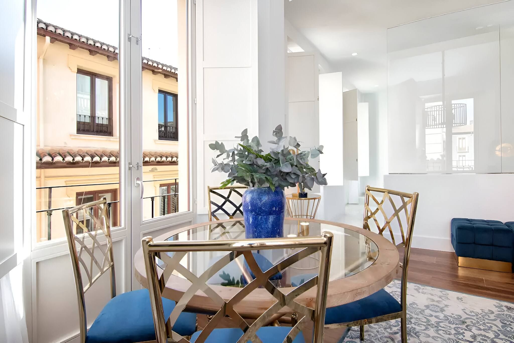 A modern dining area with a round table, chairs, and a blue vase with plants.