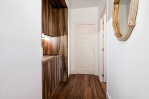 A narrow hallway with wooden flooring, a white door, and a mirror on the wall.