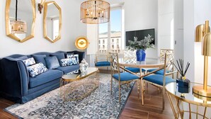 A modern living room with a blue sofa, a round coffee table, and a dining area with blue chairs and a gold table.