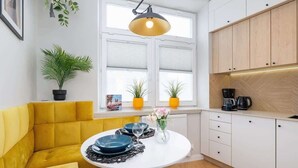 A modern kitchen with a yellow sofa, a round dining table with blue plates, and a pendant light. - Spacious Apartment | 2 Bedrooms | In the Heart of Kazimierz. (Kraków)
