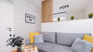 A modern living room with a grey sofa, yellow and grey cushions, a wooden sideboard with plants, and a framed picture on the wall. - Spacious Apartment | 2 Bedrooms | In the Heart of Kazimierz. (Kraków)