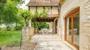 A stone house with a covered patio, outdoor seating, and a view of the surrounding greenery.