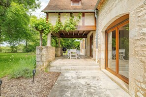 A stone house with a covered patio, outdoor seating, and a view of the surrounding greenery.