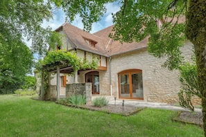 A stone house with a tiled roof, large windows, and a well-maintained garden.
