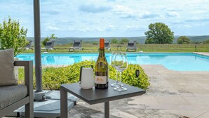 A poolside table with a bottle of wine and glasses, a water heater, and lounge chairs.