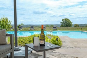 A poolside table with a bottle of wine and glasses, a water heater, and lounge chairs.