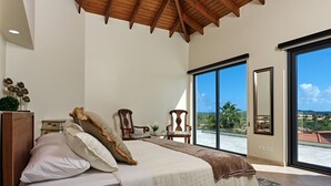 Une chambre avec un grand lit, un plafond en bois, une vue sur l’extérieur et un fauteuil.