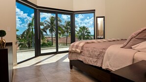 Une chambre avec une grande fenêtre, un lit et une vue sur des palmiers et des immeubles.