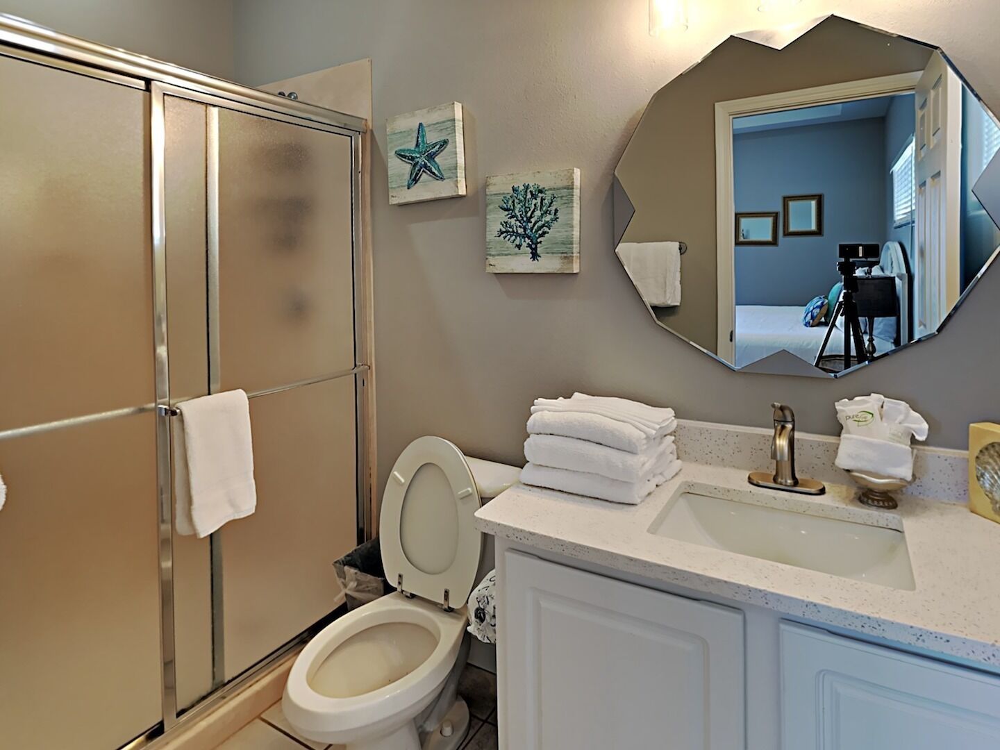 A bathroom with a shower, toilet, sink, and a large mirror.