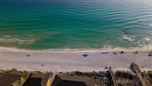 Une plage avec une eau turquoise et limpide, un rivage sablonneux, ainsi que quelques parasols et chaises de plage.