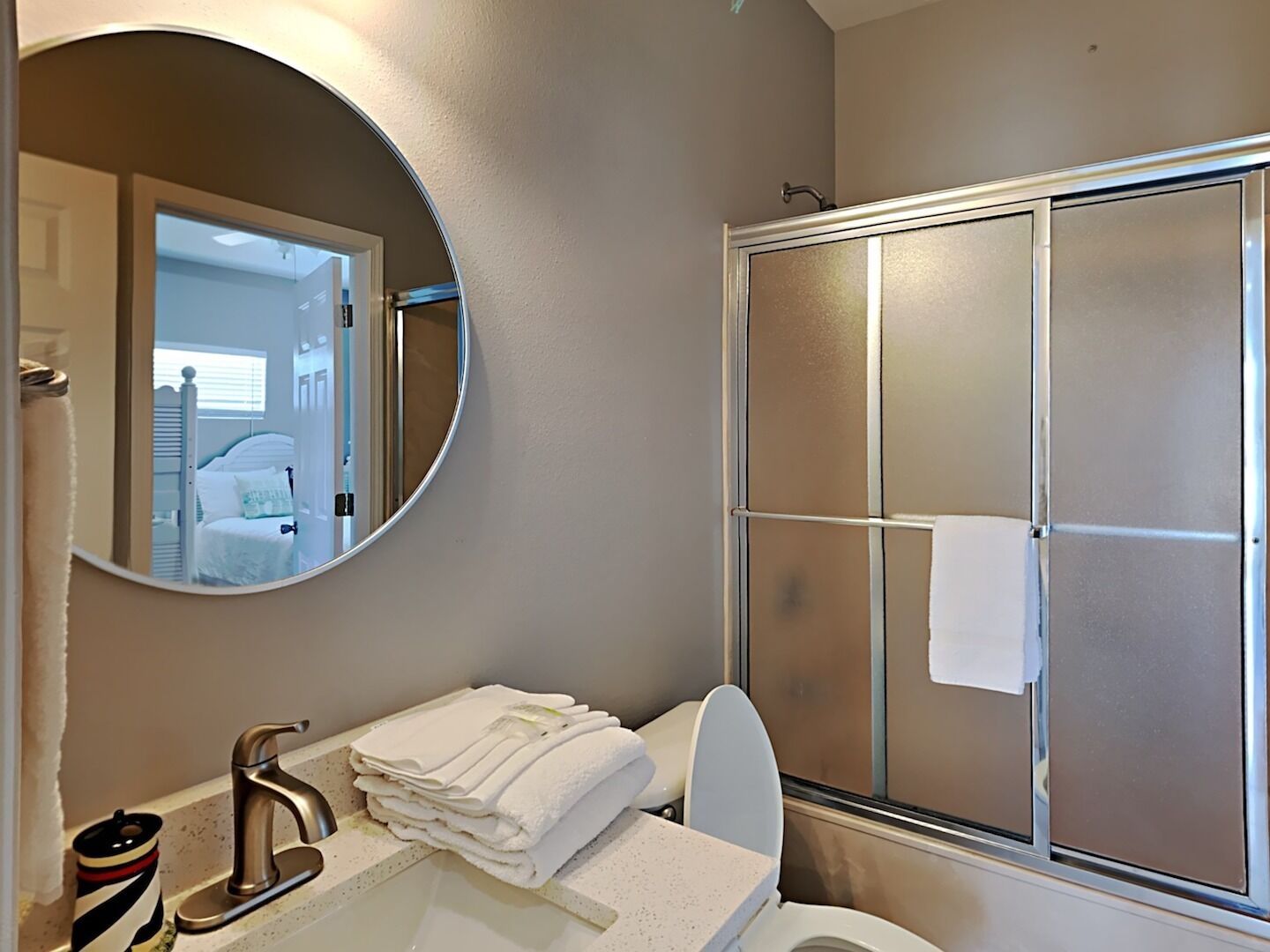 Une salle de bain avec un miroir rond, un lavabo doté d’un robinet moderne, des toilettes et une douche à parois de verre.