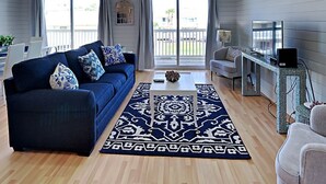 Un salon moderne avec un canapé bleu foncé, un tapis à motifs et un téléviseur posé sur un meuble en métal.