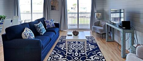 A modern living room with a dark blue sofa, a patterned rug, and a television on a metal stand.