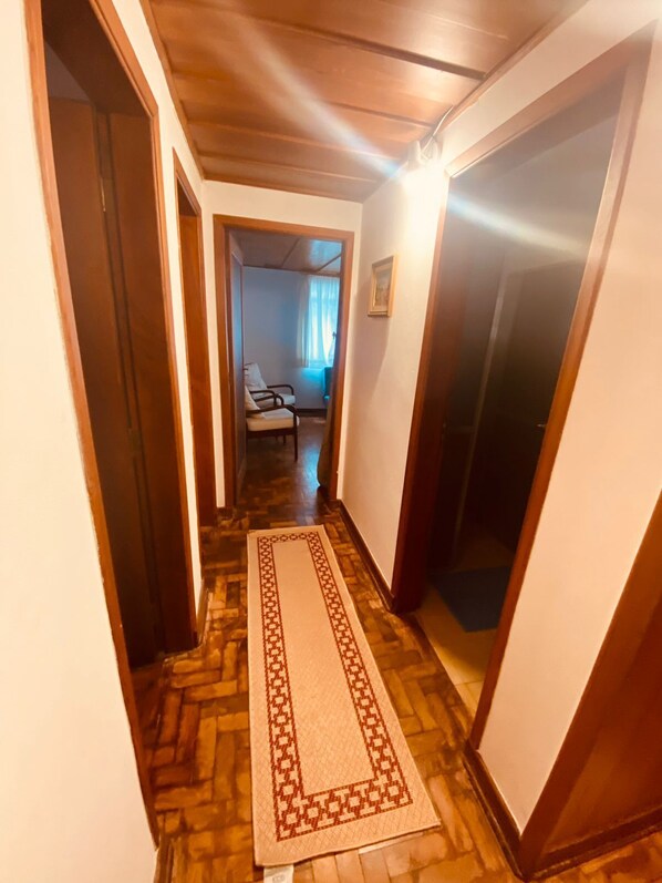 A hallway with wooden flooring, a patterned rug, and a chair in the background.