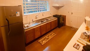 A compact kitchen with wooden cabinets, a built-in sink, and a refrigerator. - Casa Fontana (Campos do Jordão)