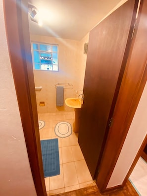 A narrow bathroom with a window, a sink, and a blue mat on the floor. - Casa Fontana (Campos do Jordão)