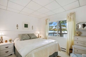 A bedroom with a bed, bedside tables, a dresser, a window with a view, and wall-mounted lamps.