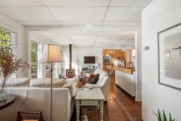 Un salon moderne avec un canapé, une table basse et un téléviseur. On aperçoit une cuisine au fond.
