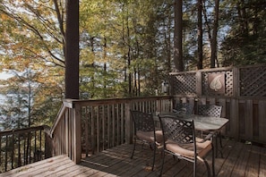 A wooden deck with a table and chairs, surrounded by trees. - Priscillas Too on Bass Lake (Mactier)