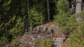 A wooden deck with chairs and a stone wall, surrounded by dense forest.