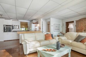 A modern living room with a sofa and a coffee table, a kitchen with white cabinets, and a dining area.