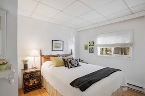 A bedroom with a bed, bedside table, lamp, and window with curtains. - Priscillas Too on Bass Lake (Mactier)