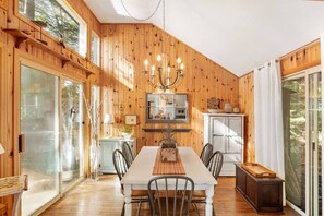 A wooden-paneled dining room with a chandelier, a table set for four, and a view through the glass door. - Priscillas Too on Bass Lake (Mactier)
