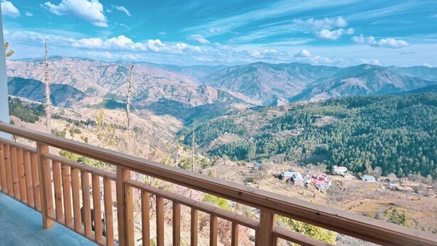 Un balcon en bois offrant une vue sur un paysage montagneux et un petit village situé en contrebas.
