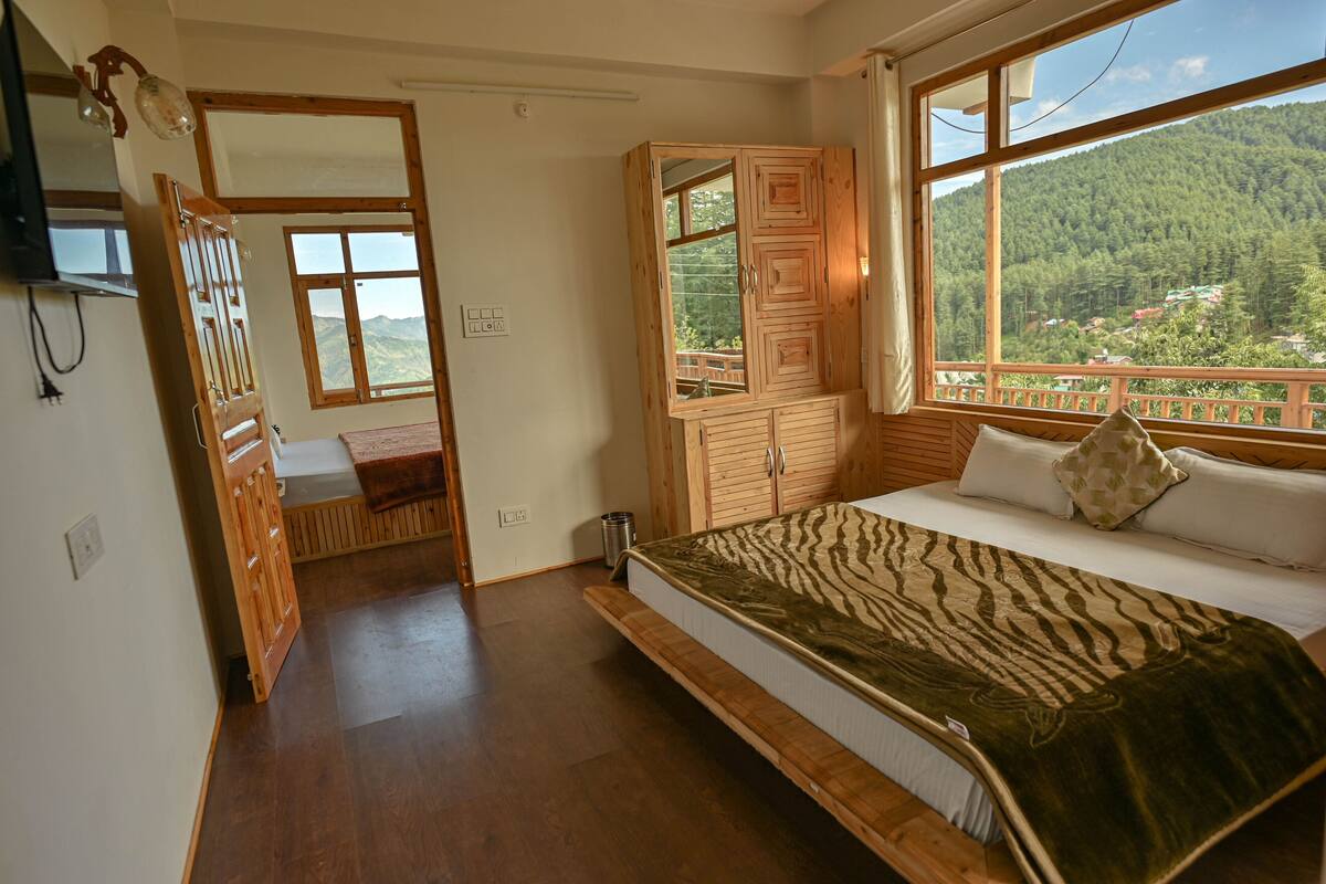 A bedroom with a bed, wooden wardrobe, and a window with a mountain view.