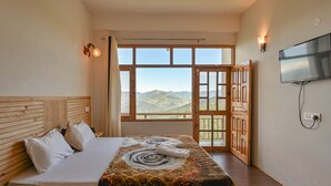Une chambre avec un grand lit, un téléviseur fixé au mur et une vue sur les montagnes par une grande fenêtre.
