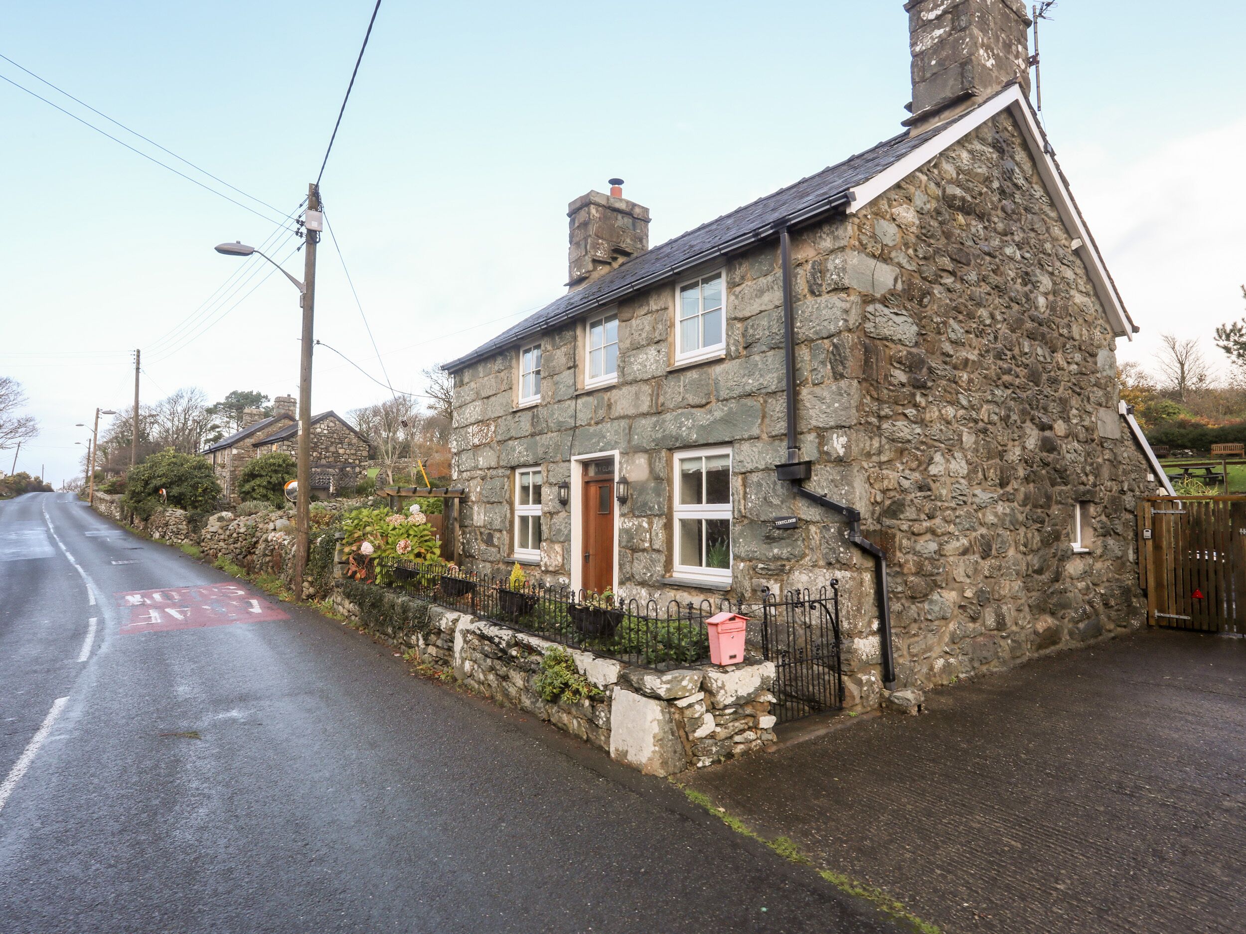 A stone house with a wooden door, a small garden, and a paved driveway.