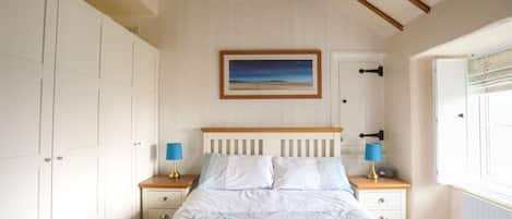 A bedroom with a bed, two bedside tables, a nightstand, a window, and a painting on the wall.