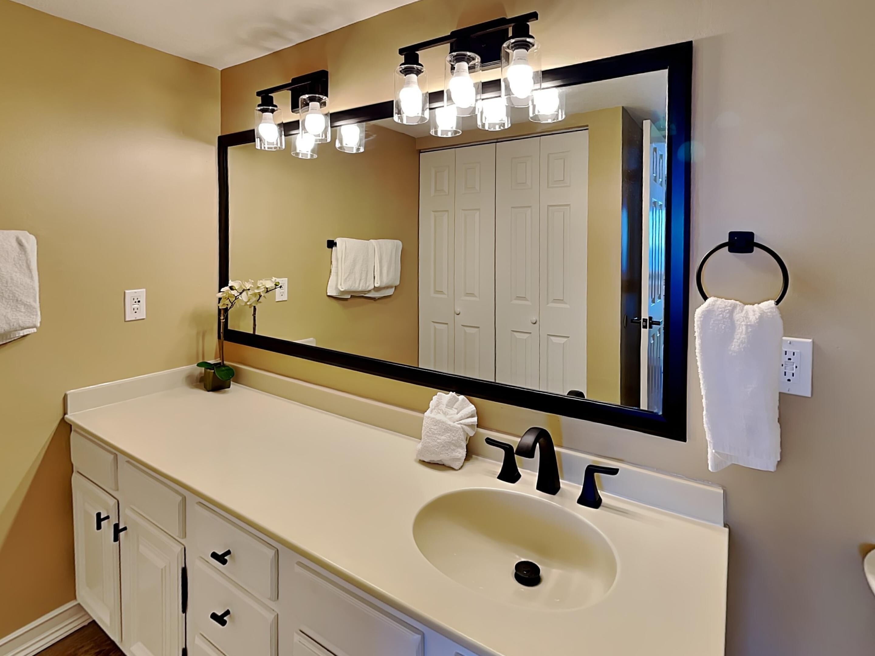 Une salle de bain avec un grand miroir, des meubles blancs, un lavabo et un porte-serviettes.