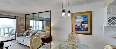 Una sala moderna con una mesa de comedor de cristal, sillas de mimbre, un sofá y un espejo grande.