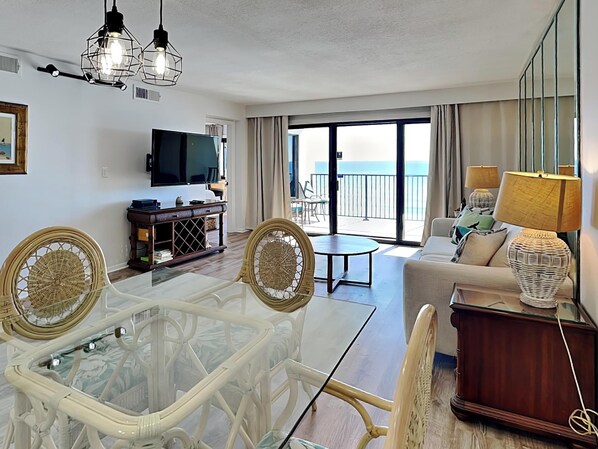 A hotel room with a balcony, a TV, a dining table, and a sofa. - Emerald Towers II by Southern Vacation Rentals (Destin)