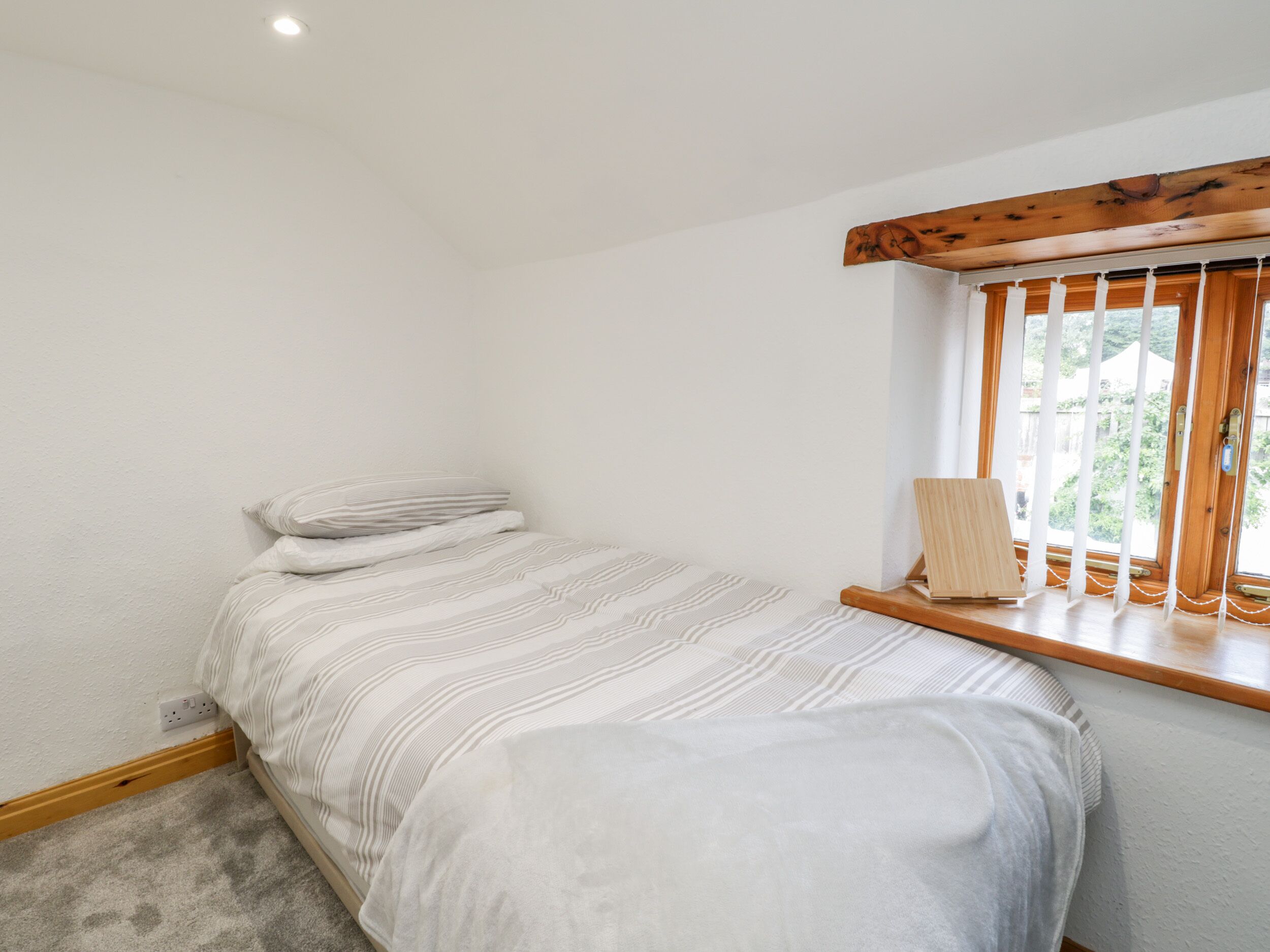 Quarto com uma cama, janela com persianas, cabeceira de madeira e uma pequena prateleira de madeira.