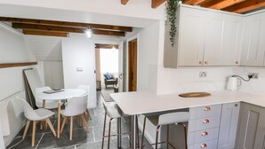 A modern kitchen with white cabinets, a marble countertop, and a bar stool. There is a dining area with a white table and chairs.