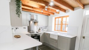 A kitchen with white cabinets, a stainless steel range hood, a window with wooden frames, and a white countertop.