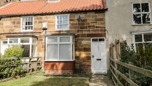 A stone house with a red-tiled roof, a white door, and a small front garden.