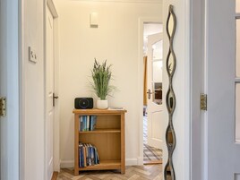 Un pasillo con una estantería de madera, una planta en maceta y un espejo decorativo.