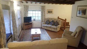 A living room with a television on a wooden stand, a beige sofa, a patterned rug, and a wooden chair. - Beautiful 15th Century Watermill - Lovely Location (Machynlleth)