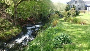 A river flowing through a lush garden with a stone building in the background. - Beautiful 15th Century Watermill - Lovely Location (Machynlleth)