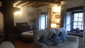 A cozy living room with a sofa, a wooden table, and a lamp. - Beautiful 15th Century Watermill - Lovely Location (Machynlleth)